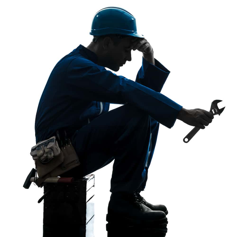 Man in construction attire sitting on a block with hand on head in defeated pose.