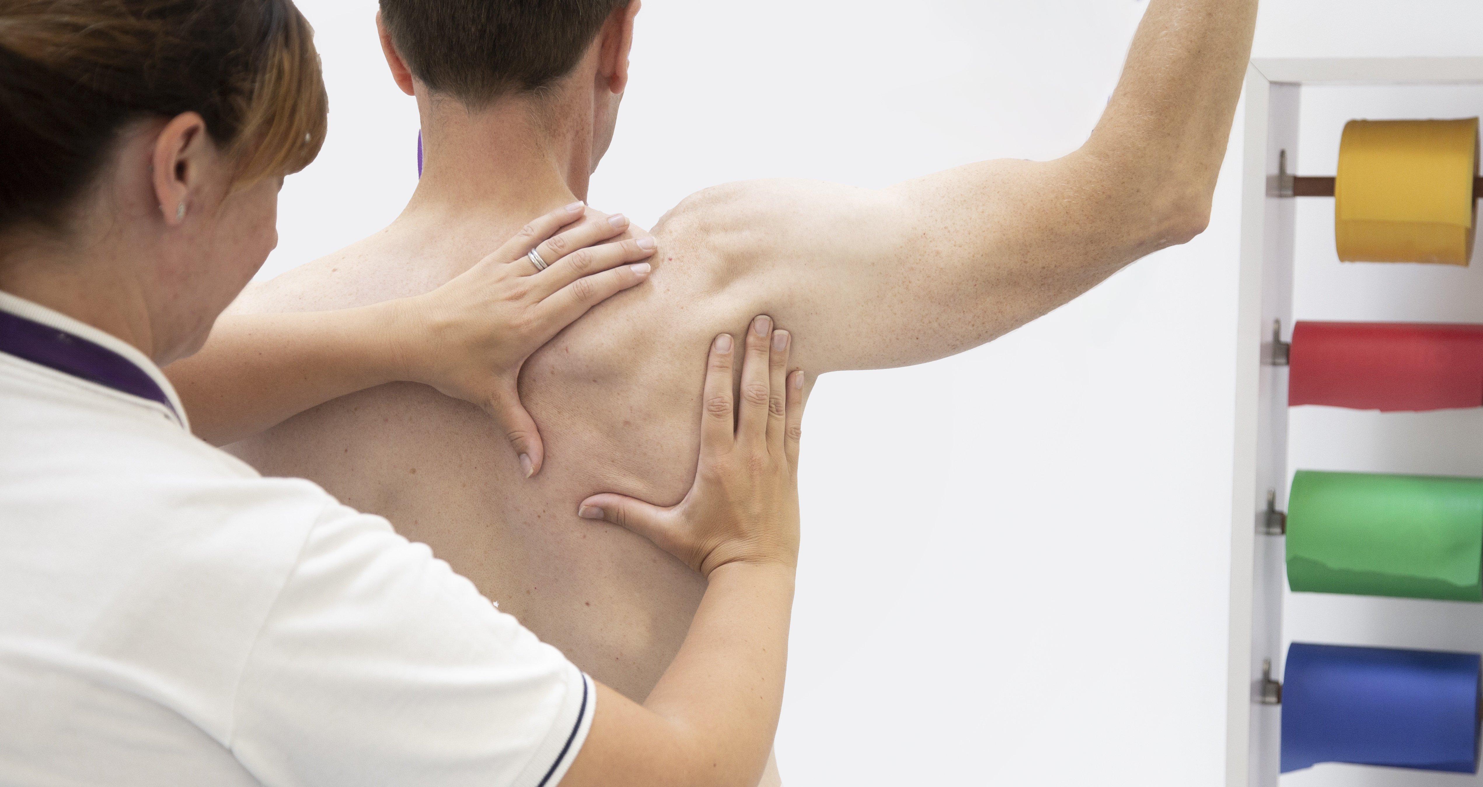 Physiotherapist performing scapula exam on patient with shoulder pain.